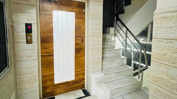 Een modern interieur met een houten deur, een trap met metalen leuningen en een lichtgekleurde betegelde vloer.