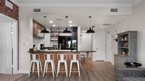 A modern kitchen with a central island, white bar stools, pendant lighting, and a rustic wooden cabinet. - First Floor Condo with Golf Course Views (Kissimmee)