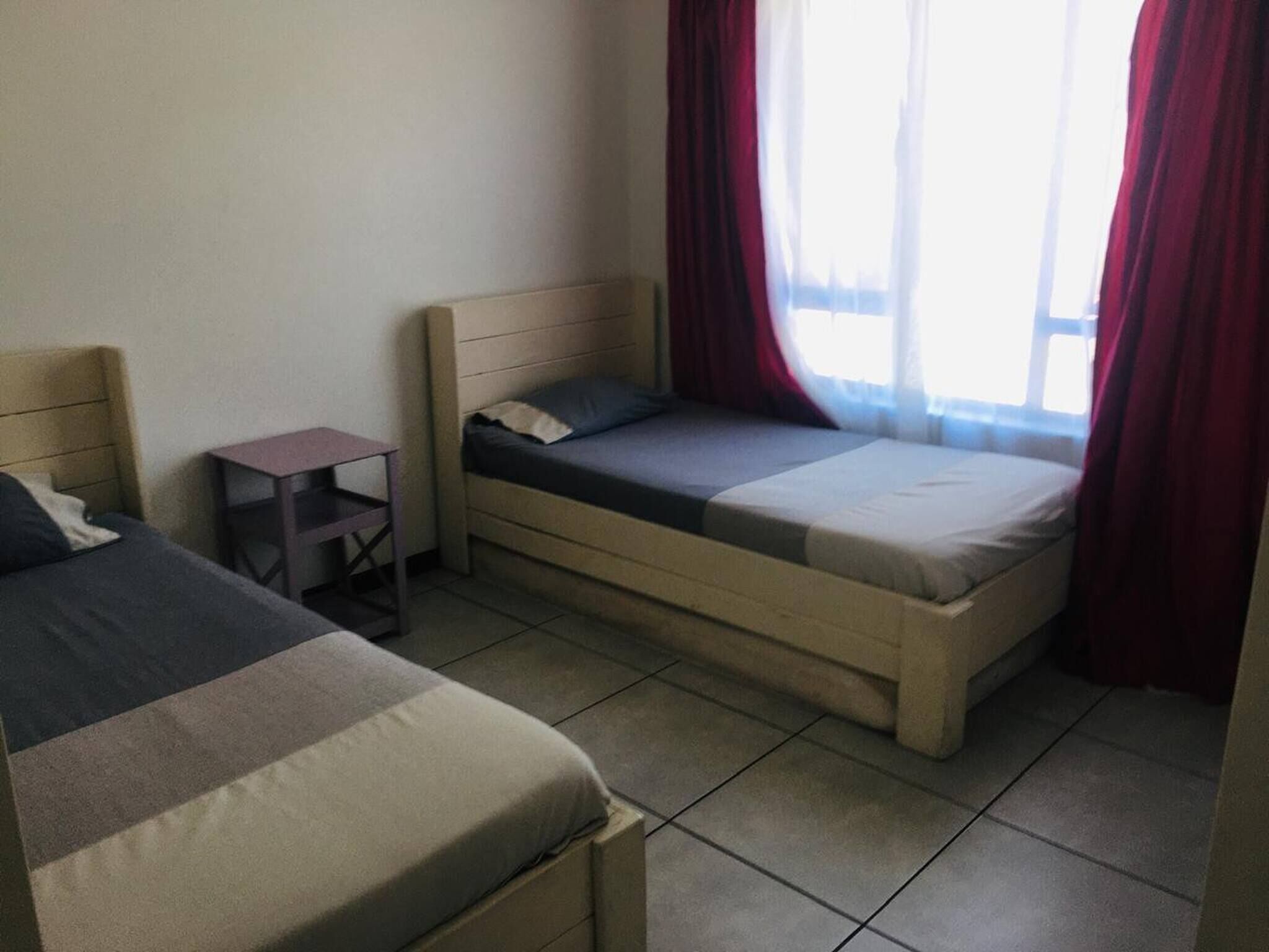 Una habitación con dos camas, una mesita y una ventana con cortinas.