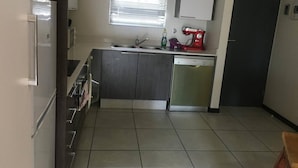 Eine kleine Küche mit Kühlschrank, Spüle, Geschirrspüler und einem Fenster mit Jalousien.