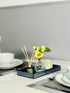 A tray with a bottle of Bergamot reed diffuser, a glass vase with yellow flowers, and a small container on a table.