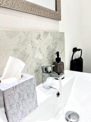 A bathroom with a marble wall, a sink with a chrome faucet, a soap dispenser, and a tissue box.