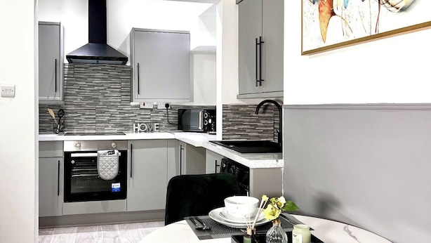 A modern kitchen with a microwave, oven, and sink. There is a dining area with a table set for two. - Stylish Spacious 1Bd Apt-kingbed-10min Heaton Park (Manchester)