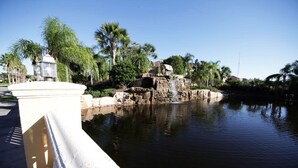 A calm water feature with a rocky island and palm trees in the background. - Themed 5Bd Paradise Palms Close to Disney w Pool 8951 (Kissimmee)