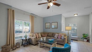 A living room with a sofa, coffee table, and chairs. There is a ceiling fan, a lamp, and a window with curtains. - Themed 5Bd Paradise Palms Close to Disney w Pool 8951 (Kissimmee)