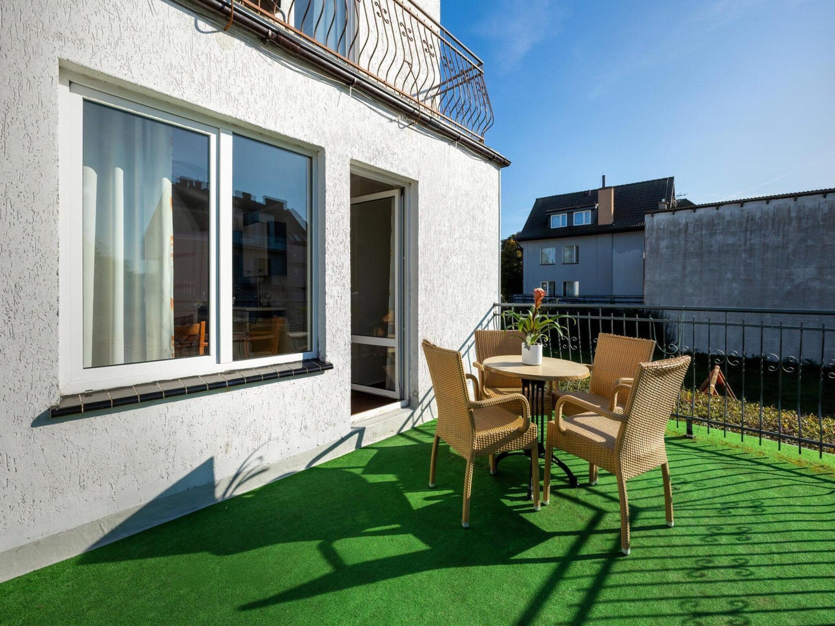 A modern house with a balcony, large windows, and a green artificial turf patio with wicker furniture.