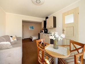 A compact living space with a kitchenette, a dining area with a table and chairs, a sofa, and a bed. - Holiday Studio Near the Beach, Rewal (Rewal)