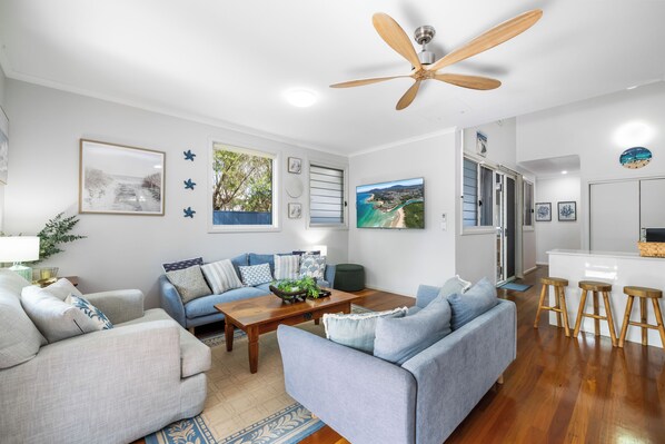 A modern living room with a ceiling fan, a sofa set, a coffee table, and a TV mounted on the wall.