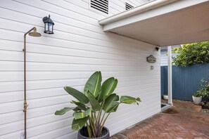 A white house exterior with a potted plant, a metal pipe, and a sign indicating a rainwater system.