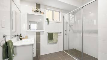 A modern bathroom with a glass shower enclosure, a white sink with a mirror above, and a green towel hanging on the wall.