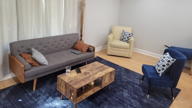 Ein Wohnzimmer mit grauem Sofa, einem Holztisch, einem blauen Sessel und einem gemusterten Sessel.
