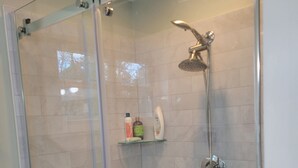 Eine begehbare Dusche mit Glaswänden, einer Handbrause und einem am Wand montierten Wasserhahn.