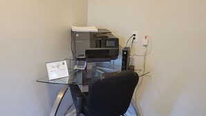Ein moderner Arbeitsplatz mit einem Glastisch, einem schwarzen Bürostuhl und einem HP-Drucker.