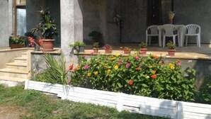 A covered outdoor area with a concrete floor, potted plants, and white plastic chairs. - Gabala Dreams, charming 2 bedroom villa, (Vandam)