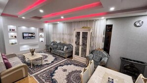 A modern living room with a grey sofa, a white armchair, a coffee table, a TV mounted on the wall, and a fireplace. - Gabala Dreams, charming 2 bedroom villa, (Vandam)