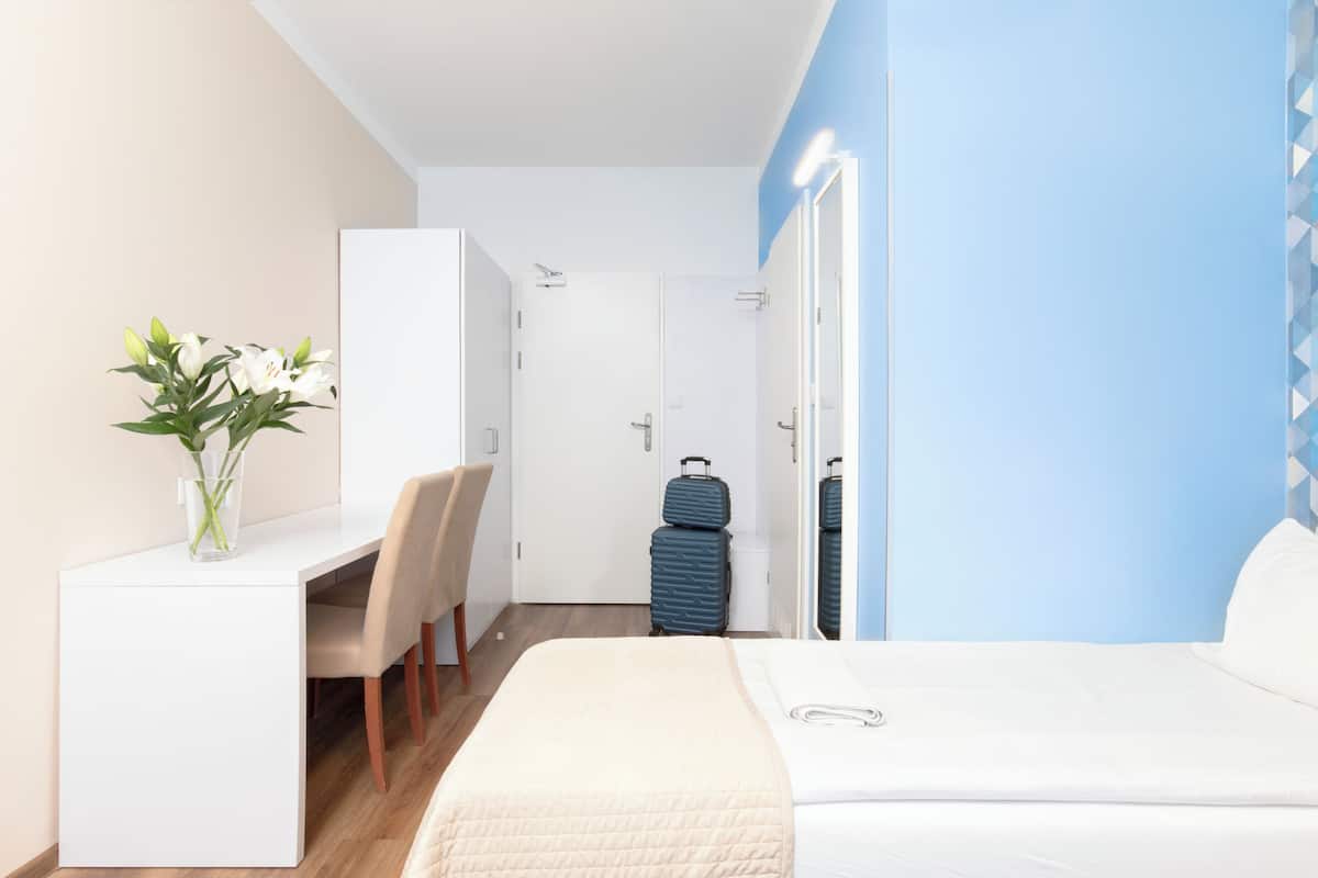 Ein Hotelzimmer mit Bett, Schreibtisch, Stuhl, Spiegel und Koffer.