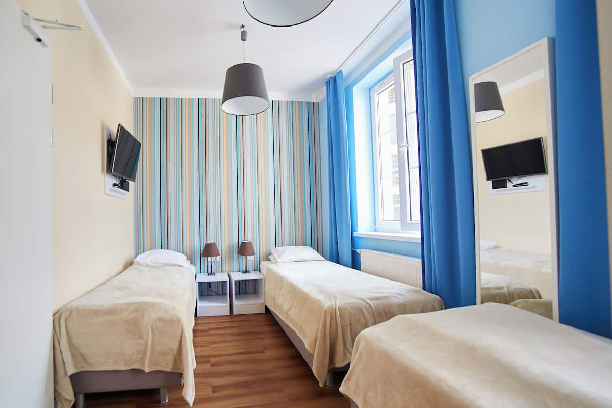 Ein Hotelzimmer mit zwei Einzelbetten, einem kleinen Tisch mit Stühlen, einem an der Wand befestigten Fernseher und einem Fenster mit Vorhängen.
