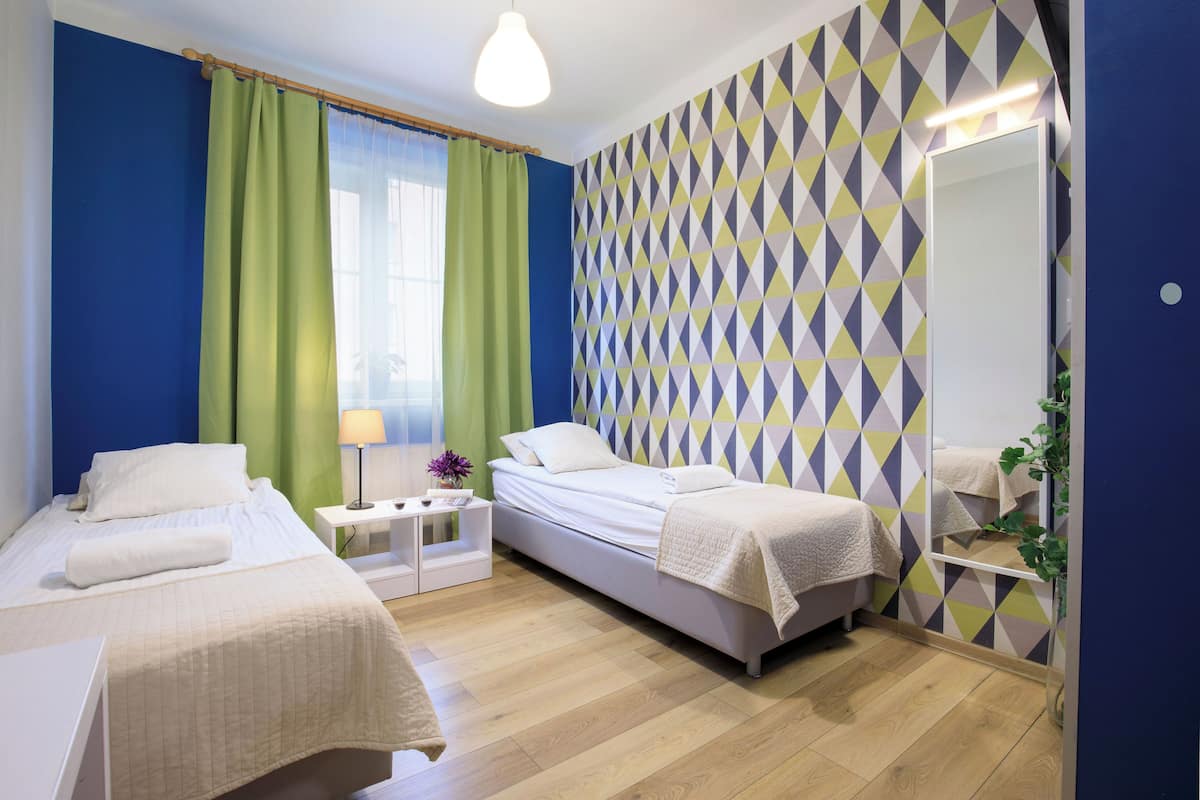 Ein Hotelzimmer mit zwei Betten, einem Nachttisch mit Lampe, einem Spiegel und einer Wand mit geometrischem Muster.