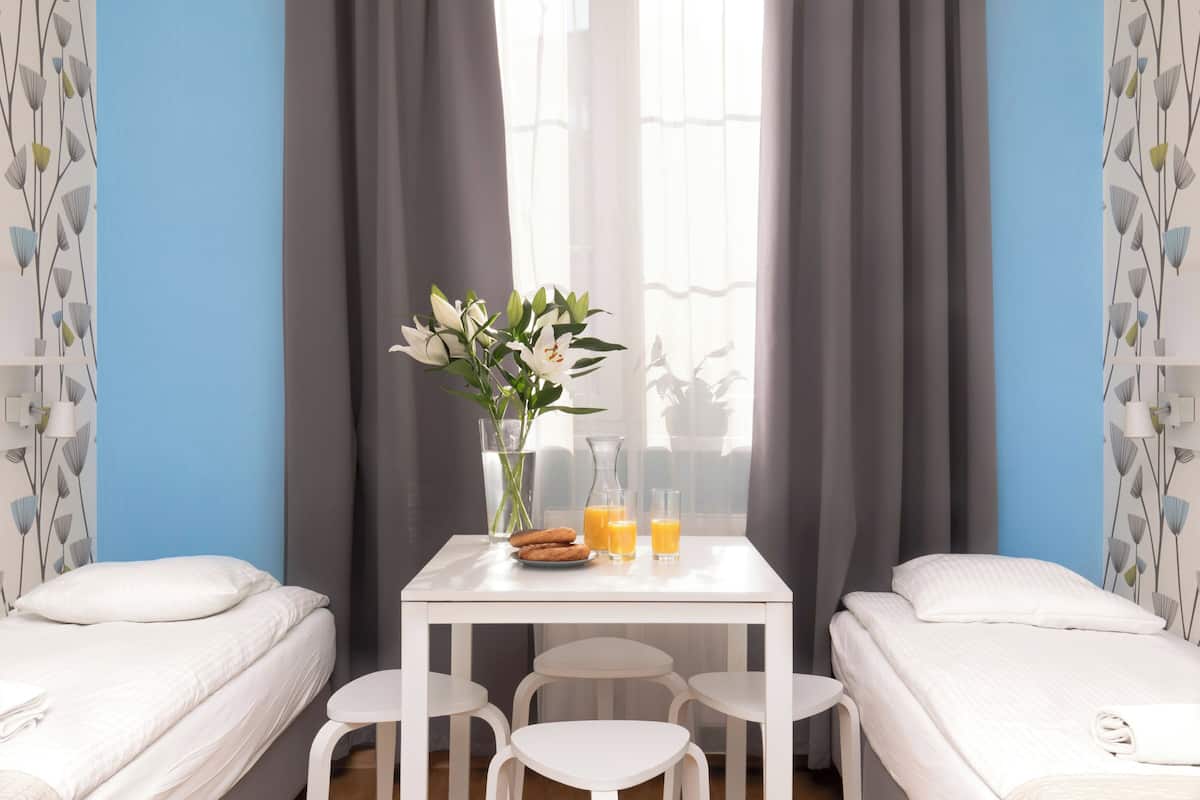 Ein Hotelzimmer mit zwei Einzelbetten, einem kleinen weißen Tisch mit Blumenvase, zwei Gläsern Orangensaft und einer kleinen Teller Kekse.