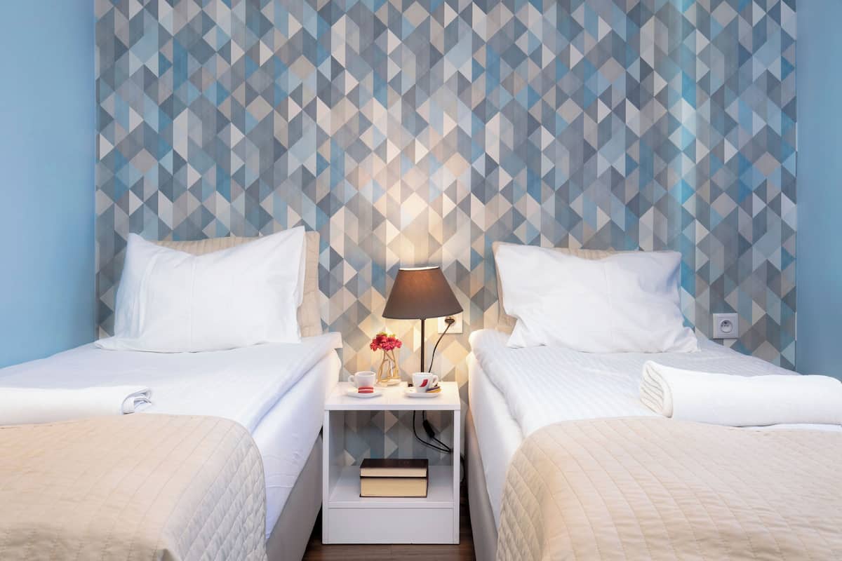 Ein Hotelzimmer mit zwei Betten, einem Nachttisch mit Lampe und einer Wand mit geometrischem Muster.