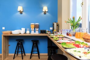 A breakfast bar with various food items, two wall-mounted lamps, and a window with a view. - Premium Hostel (Kraków)