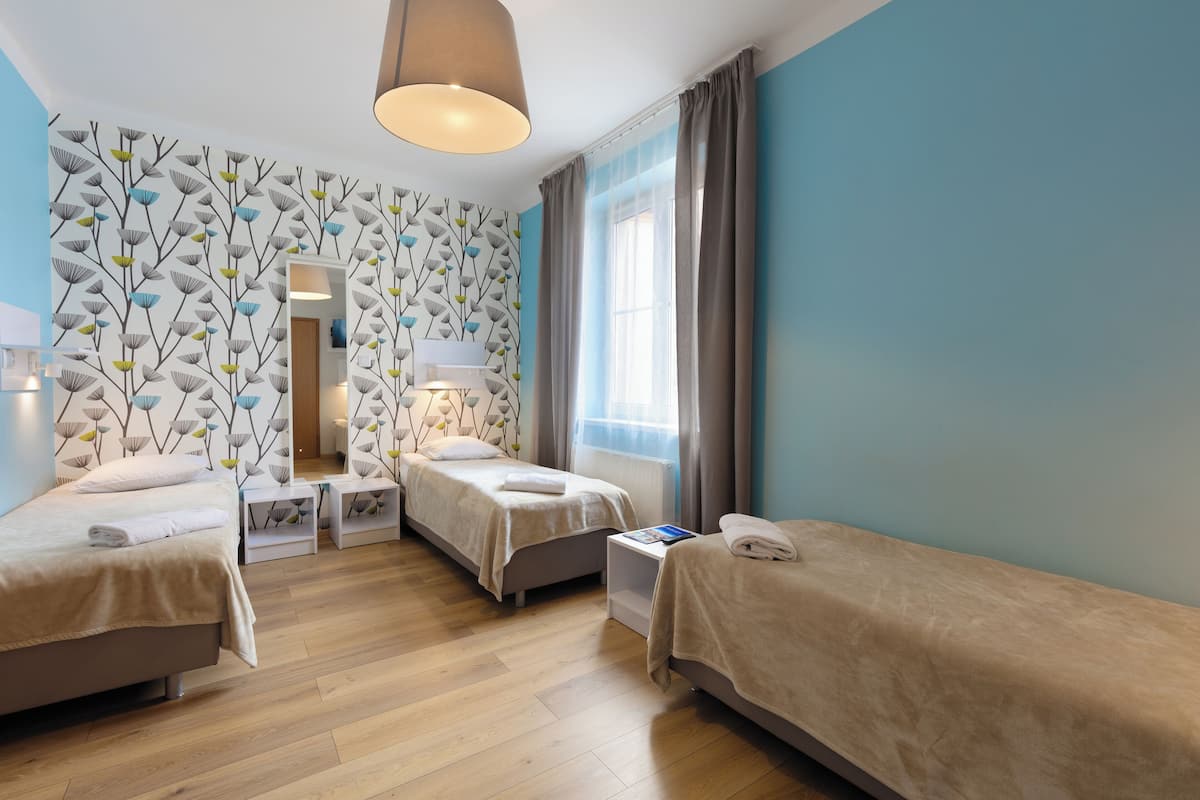 Ein Hotelzimmer mit zwei Betten, Holzboden, einem gemusterten Wand und einem Fenster mit Vorhängen sowie einer Pendelleuchte.