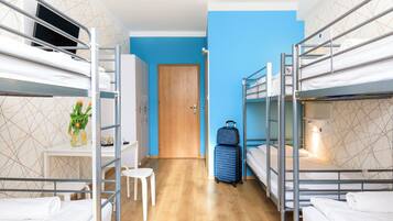 A hotel room with bunk beds, a desk with a chair, a small stool, a wooden door, and a suitcase.
