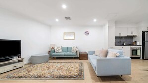 Un salon moderne avec un téléviseur à écran plat, deux canapés, un tapis à motifs et une cuisine en arrière-plan.