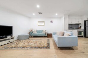 A modern living room with a flat-screen TV, two sofas, a patterned rug, and a kitchen in the background. - Idyllic and Spacious apartment near Trendy Zetland (Waterloo)