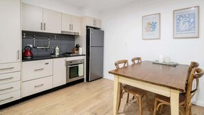 Une cuisine moderne avec des meubles blancs, un réfrigérateur en acier inoxydable et une table à manger en bois, accompagnée de chaises.