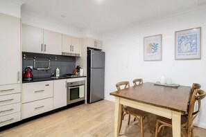 A modern kitchen with white cabinets, a stainless steel refrigerator, and a wooden dining table with chairs. - Idyllic and Spacious apartment near Trendy Zetland (Waterloo)