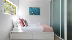 Une chambre à coucher moderne avec un lit, des oreillers, une couverture, une fenêtre et un tableau au mur.