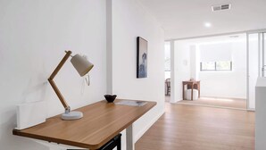 Une chambre moderne avec un bureau en bois, une lampe de bureau, un tableau encadré et une fenêtre.