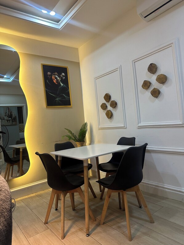 Zona pranzo con tavolo bianco, sedie nere e una pianta in vaso.