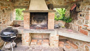 Een buitenkeuken van baksteen met een barbecue, een stenen haard en een schoorsteen.