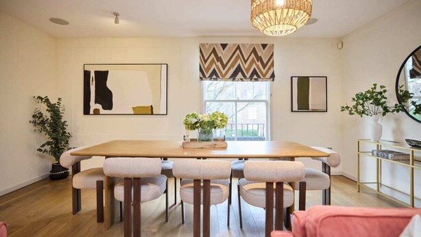 Un comedor con mesa de madera y seis sillas, un ventanal con cortina a cuadros en zigzag y una lámpara colgante de mimbre.