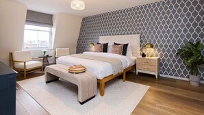 A modern bedroom with a large bed, bedside tables, a chair, and a potted plant.