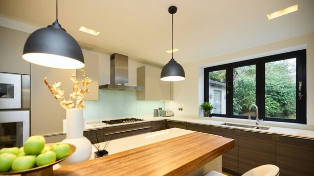 A modern kitchen with a central island, pendant lighting, and a view of greenery outside.