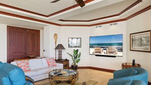 Un salón con sofá, sillones, una mesa de centro y un televisor grande mostrando una playa.