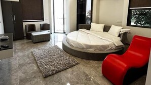 Ein modernes Schlafzimmer mit einem runden Bett, einem roten Sessel, einem Deckenventilator und einem großen Fenster.