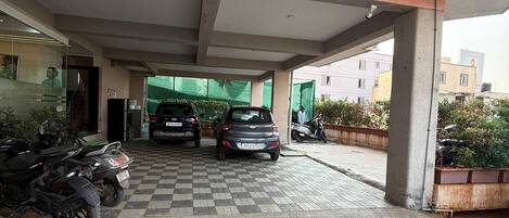 A covered parking area with a checkered floor, a few parked vehicles, and a building entrance with a glass door.