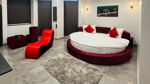 Ein modernes Schlafzimmer mit einem runden Bett, rot-weißer Bettwäsche, einem Deckenventilator und einem großen Fenster.