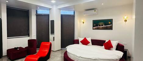 Un dormitorio moderno con cama redonda, ropa de cama roja y blanca, ventilador de techo y una ventana grande.