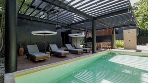 A covered outdoor pool area with lounge chairs and umbrellas.