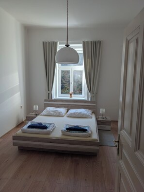 A bedroom with a bed, bedside tables, a hanging light fixture, and a window with curtains.