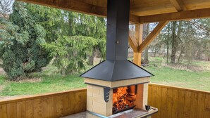 Een houten constructie buiten met een ingebouwde barbecue, een vuilnisbak en uitzicht op een bebost gebied.