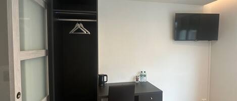 Una habitación pequeña y moderna con escritorio, armario negro con puerta de cristal, perchero y televisor de pantalla plana montado en la pared.