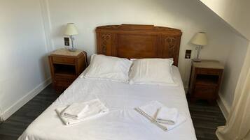 A neatly made bed with white linens and two folded towels, wooden headboard, two bedside tables with lamps, and a wooden floor.