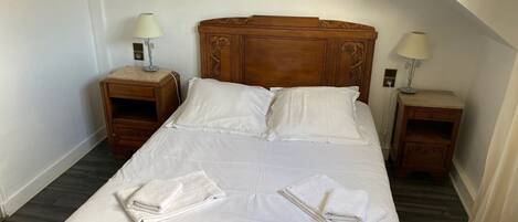 A neatly made bed with white linens and two folded towels, wooden headboard, two bedside tables with lamps, and a wooden floor.