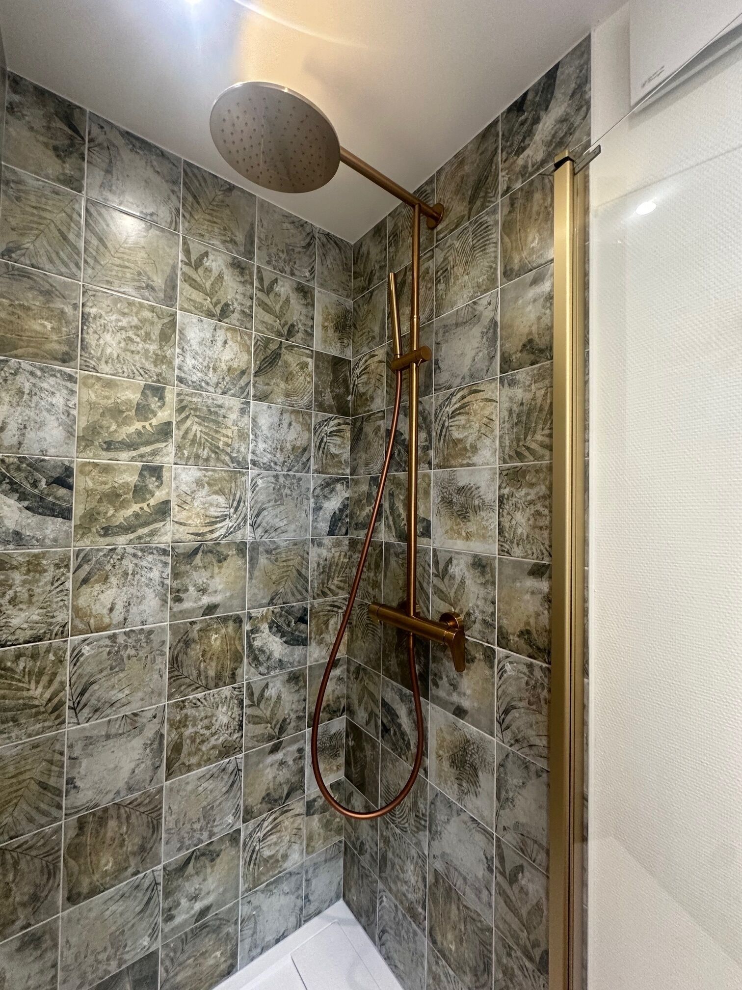 A shower with a handheld showerhead and a rain shower head, surrounded by marble-patterned tiles.